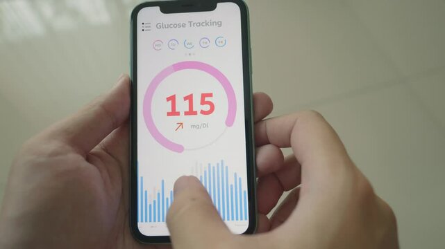 A close-up view of a smartphone showing a glucose tracking app. The screen displays glucose levels, with the current measurement indicating 115 mg/DL, surrounded by graphs and indicators for health mo