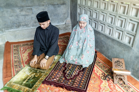Picture of Muslim man with his wife posing prostration while doing Salat in the home