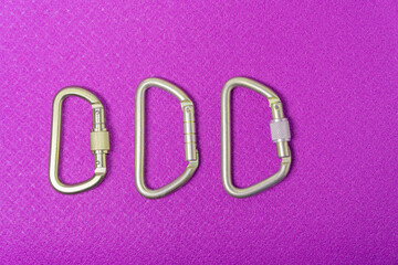 Three steel climbing carabiners on a purple touristic mat
