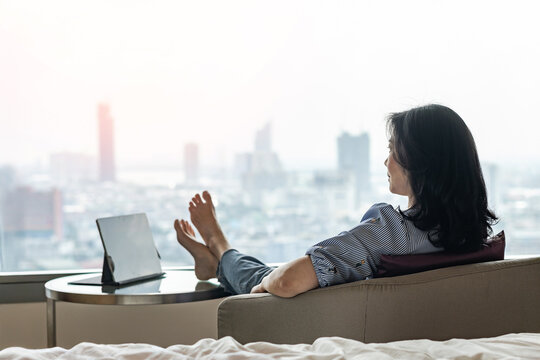 Life quality concept with business woman rear view relaxing sitting in rest on cozy chair staying in modern city hotel guest room or luxury home living room with computer laptop