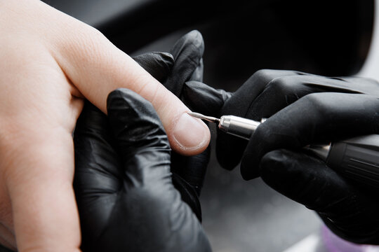 Closeup professional manicure for man by machine in beauty salon, black background