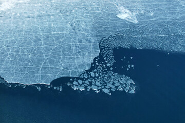 Ice with cracks and single ice floes in the water. Time of ice melting in spring. Abstract nature background. Aerial photography
