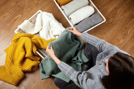 A young woman puts a knitted sweater in a metal laundry basket. The concept of putting things in order, cleaning, creating disorder, and organizing space. Top view