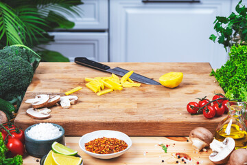 Healthy eating, cooking, food blogging background. Raw potatoes cut into strips and knife on oak cutting board with vegetables, herbs and spices on cozy kitchen with wooden table, kitchenware 