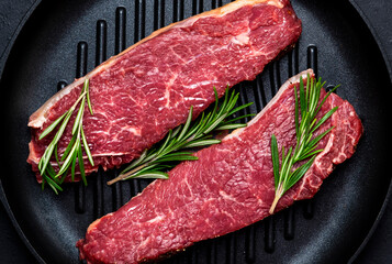 Raw beef sirloin steaks with medium mamory with rosemary on grill pan. Black background, top view