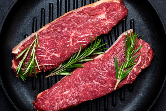 Raw beef sirloin steaks with medium mamory with rosemary on grill pan. Black background, top view