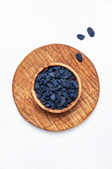 Organic sun dried black blue raisins in wooden bowl on white background, top view