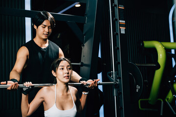 Asian woman guy a squat exercise legs heavy weights with a barbell with the assistance of a trainer...