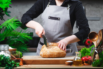 Chef cutting white bread. Cozy kitchen with wooden table, kitchenware and ingredients for cooking. Homemade baking, cooking, food blogging