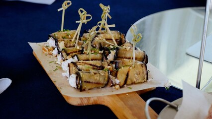 Grilled eggplant rolls stuffed with creamy cheese, topped with crunchy walnuts and verdant herbs, resting on rustic wooden surface