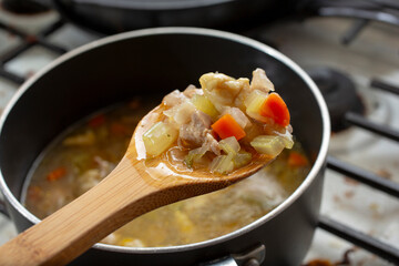 A view of a wooden spoon scooping contents from a stockpot of chicken soup.
