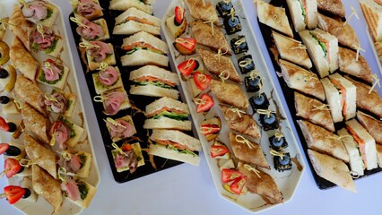 Varied platters holding delicate mini sandwiches, rolled crepes, and canapes, presenting...