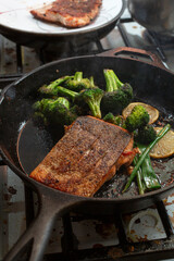 A view of a salmon fillet and broccoli cooking in a cast iron skillet.