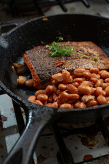 A view of a salmon filet and pinto beans in a cast iron skillet.