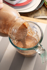 A view of a large mason jar pouring bananamilk into a glass measuring cup.