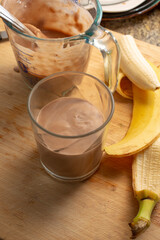 A view looking of a glass of chocolate bananamilk next to a banana.