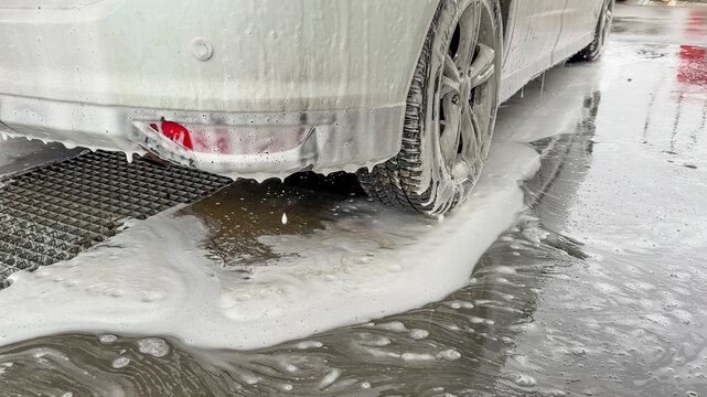 A white car undergoes a thorough wash with suds at a car wash station, addressing vehicle cleanliness and maintenance