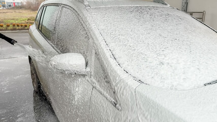 A car is being thoroughly cleaned with foam spray at a car wash, emphasizing vehicle maintenance and cleanliness