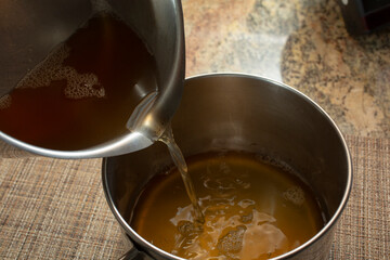 A view of one pot pouring bone stock into another pot.