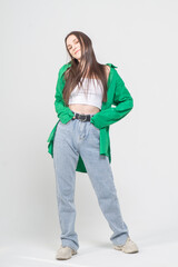 Cute young girl in green shirt and blue jeans posing on a white background