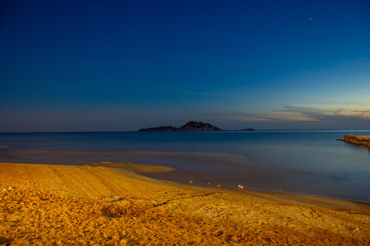 Tranquil seascape featuring a beach in the foreground, calm water, and a distant island under a night sky.Arillas, Corfu island, greece, 
