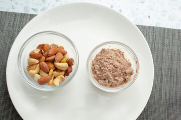A top down view of a bowl of protein powder, and a bowl of mixed nuts.