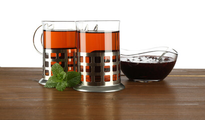 Glasses of aromatic tea in holders, mint and jam on wooden table against white