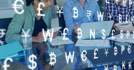 Image of currency icons over diverse colleagues using laptop in office
