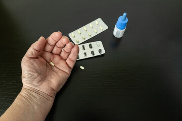 A hand holds a tablet, and a bottle of nasal drops is on the table.