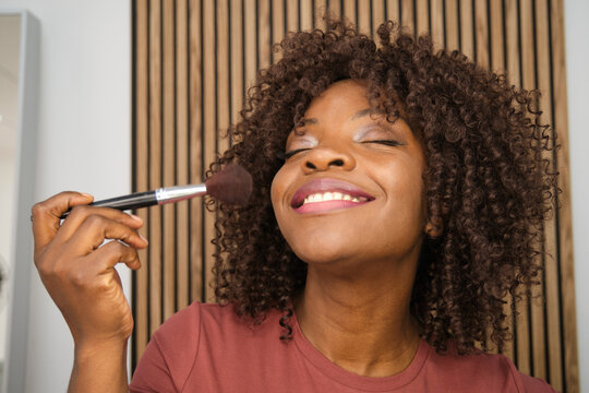 Smiling woman applying blush with makeup brush