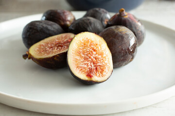 A view of some black mission figs, featuring one that is halved.