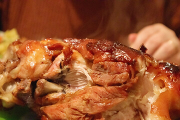 
oven-baked pork leg with crispy skin, served on a plate with vegetables and garnished with herbs.