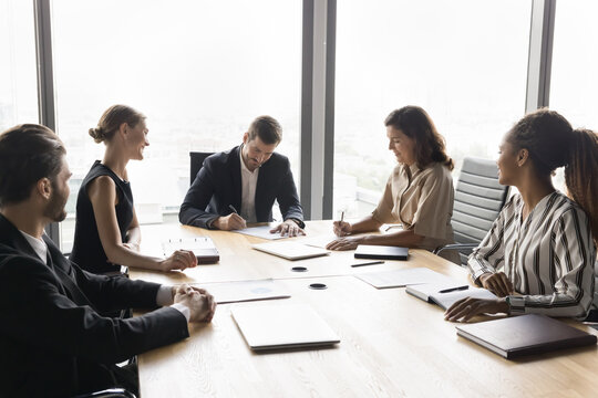 Group of diverse business partners, stakeholders signing contracts sit at table in office, put signatures on legal documents papers after successful negotiations, establish partnership, make agreement