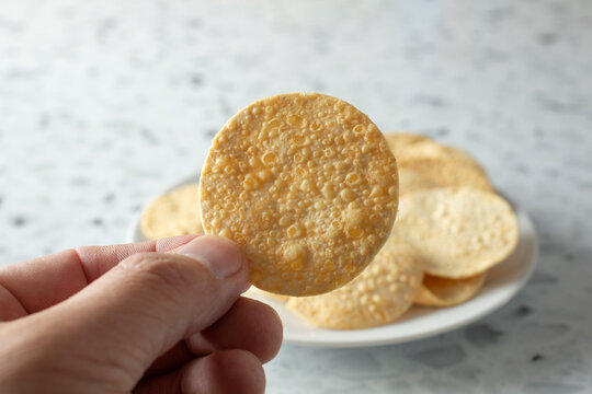 A view of a hand holding a papadam chip.