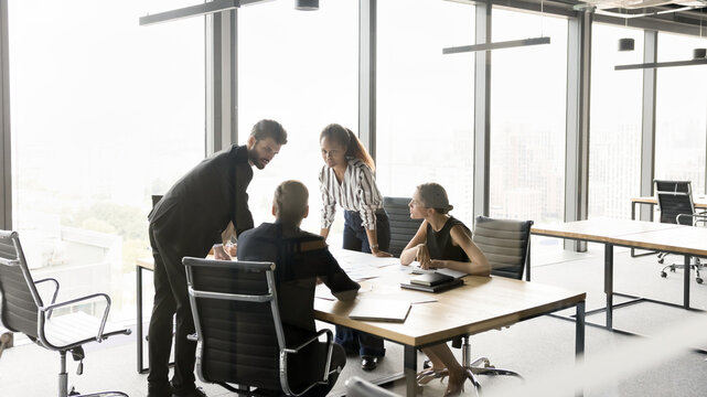 Group of multiethnic businesspeople gathered around conference table to review papers, analyzing sales statistics, share decisions, strategy and joint project updates, doing paperwork and forecasting