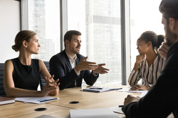 Group of business professionals gathered in modern board room, engaged in serious discussion,...