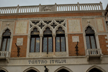 Obraz premium Teatro Italia is a historic building in Venice, Italy. Its stunning Gothic-style windows and intricate details reflect Venetian elegance, and the warm tones of the brick glow under the cloudy skies.