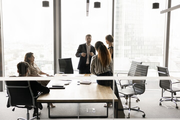 Five multiethnic staff members take part in morning briefing in high-rise office building behind closed doors, gathered together for teamwork, opinion sharing, strategizing and planning cooperation