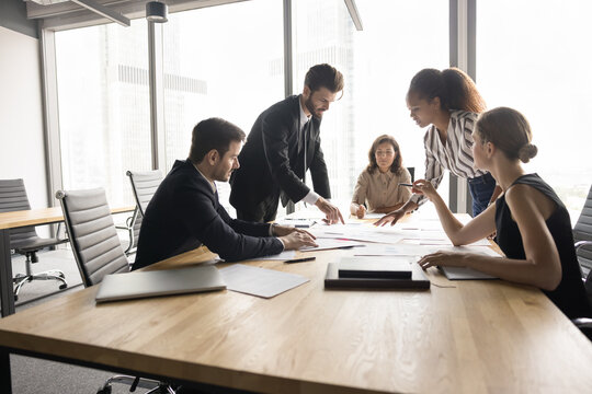 Strategic project evaluation meeting. Group of multiethnic businesspeople, marketing experts take part in briefing, review documents related to upcoming project, share ideas, researching, forecasting - Powered by Adobe