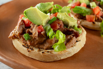 A closeup view of a carnitas sope, on a plate.