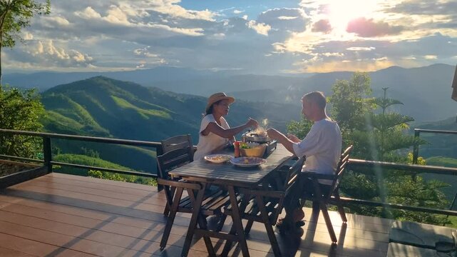 Couple enjoys a delightful meal while overlooking the stunning rice fields of Chiang Mai, Thailand. The sunset paints the sky with vibrant hues, creating a romantic atmosphere.