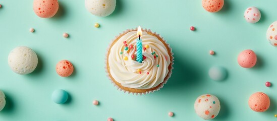 Colorful birthday cupcake with a candle surrounded by festive decorations on a mint background