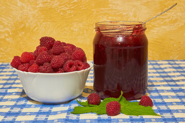 jar of raspberry jam and fresh berries, homemade raspberry jam on a table with a blue tablecloth