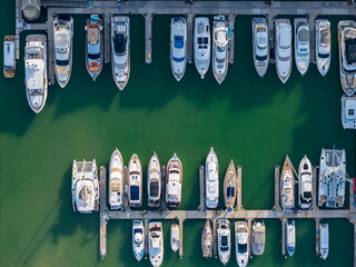 Aerial top view of a marina with luxury yachts and boats docked in neatly arranged rows.