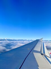 View from airplane window of a plane in flight with wing.  View above the clouds with the Swiss apls in the distance.  Bright blue, clear, sunny sky.  No people, copy space.