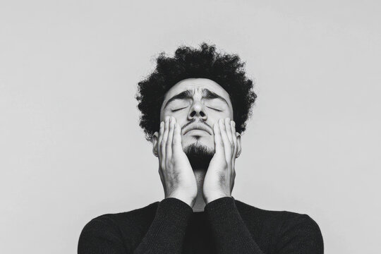 Black and white portrait of a man with closed eyes holding his face, expressing deep emotion