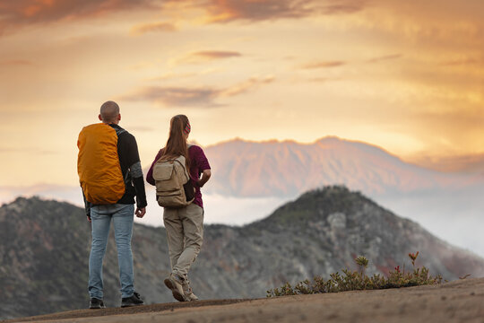 Couple of young hikers with backpacks are standing at mountain top and enjoys sunrise and great view