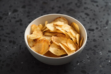 Organic potato chips with black pepper in white ceramic bowl on concrete background