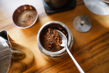 Person filling funnel of a moka pot with ground black coffee in a home kitchen. The process of...
