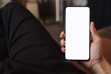 Man hold smartphone with white screen in his hand sitting on a couch in home environment